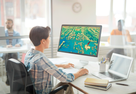 Das Bild zeigt eine Frau an ihrem Computerarbeitsplatz. Sie arbeitet am Computer, wo sie eine Karte geöffnet hat.