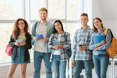 Das Bild stellt 5 junge Menschen mit Rucksack und Schulsachen in der Hand dar.