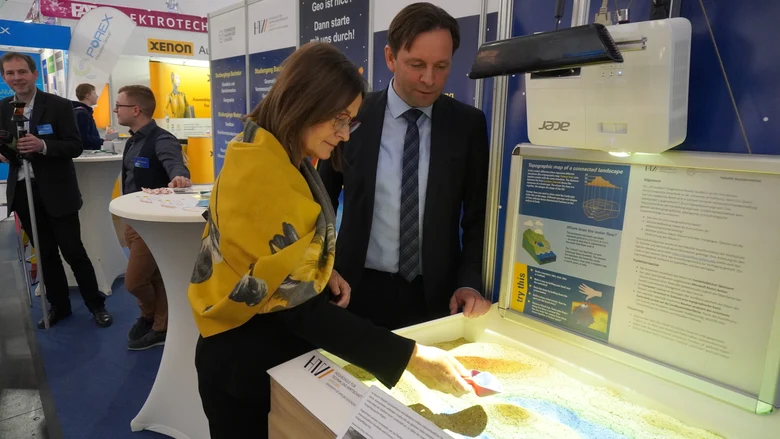 Ronny Zienert und Barbara Meyer testen etwas mit Sand und einer kleinen Schaufel aus.